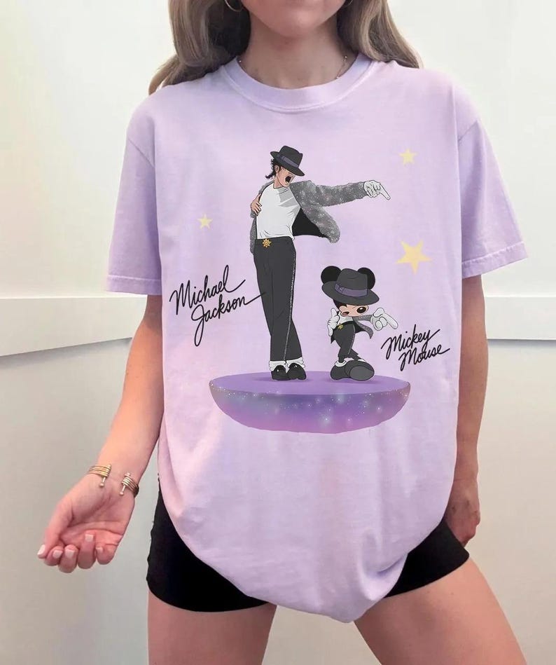 Puede incluir: Una camiseta de color lila claro con un gr&aacute;fico de Michael Jackson y Mickey Mouse. La ilustraci&oacute;n muestra a Michael Jackson con sombrero y traje negro, y a Mickey Mouse con un atuendo similar. Las palabras "Michael Jackson" y "Mickey Mouse" est&aacute;n escritas en cursiva.