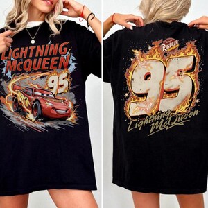 Puede incluir: Camiseta negra con un dise&ntilde;o de Rayo McQueen de la pel&iacute;cula Cars. El frente muestra a McQueen con el n&uacute;mero 95, y la parte trasera presenta el n&uacute;mero 95 entre llamas, con el texto "Lightning McQueen".