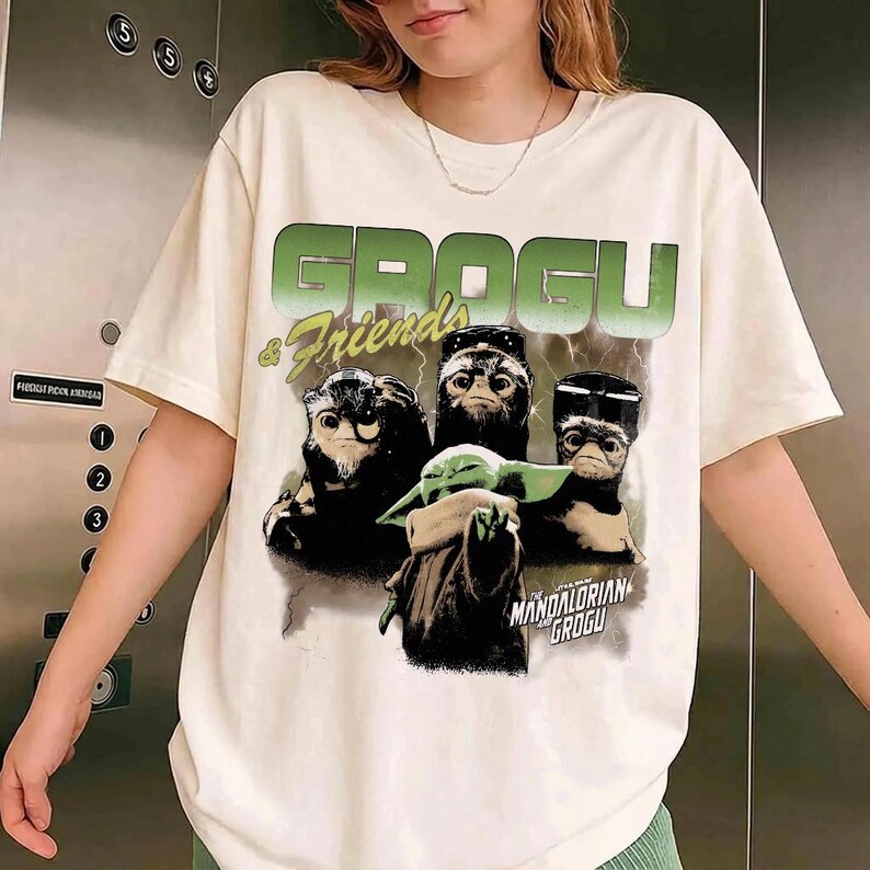 Pu&ograve; includere: T-shirt color crema con la scritta "GROGU & Friends" in verde e bianco. La grafica include Grogu e altre tre creature. Le parole "MANDALORIAN GROGU" sono stampate sotto i personaggi.