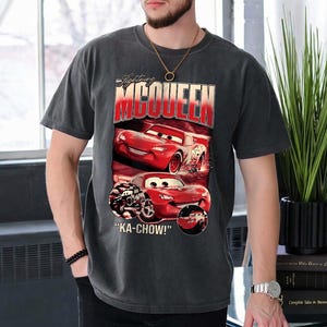 Puede incluir: Camiseta gris oscuro con Lightning McQueen de la pel&iacute;cula Cars. El dise&ntilde;o incluye im&aacute;genes del coche de carreras rojo y el texto "Lightning McQueen" y "KA-CHOW!". La camiseta tiene un aspecto vintage.