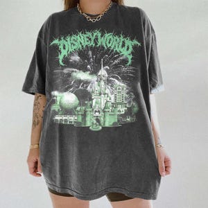 K&ouml;nnte beinhalten: Dunkelgraues T-Shirt mit einem verwaschenen "DISNEY WORLD"-Aufdruck in Neongr&uuml;n. Das Design zeigt ein Schloss, Feuerwerk und Parkelemente. Das Shirt hat kurze &Auml;rmel und eine lockere Passform.