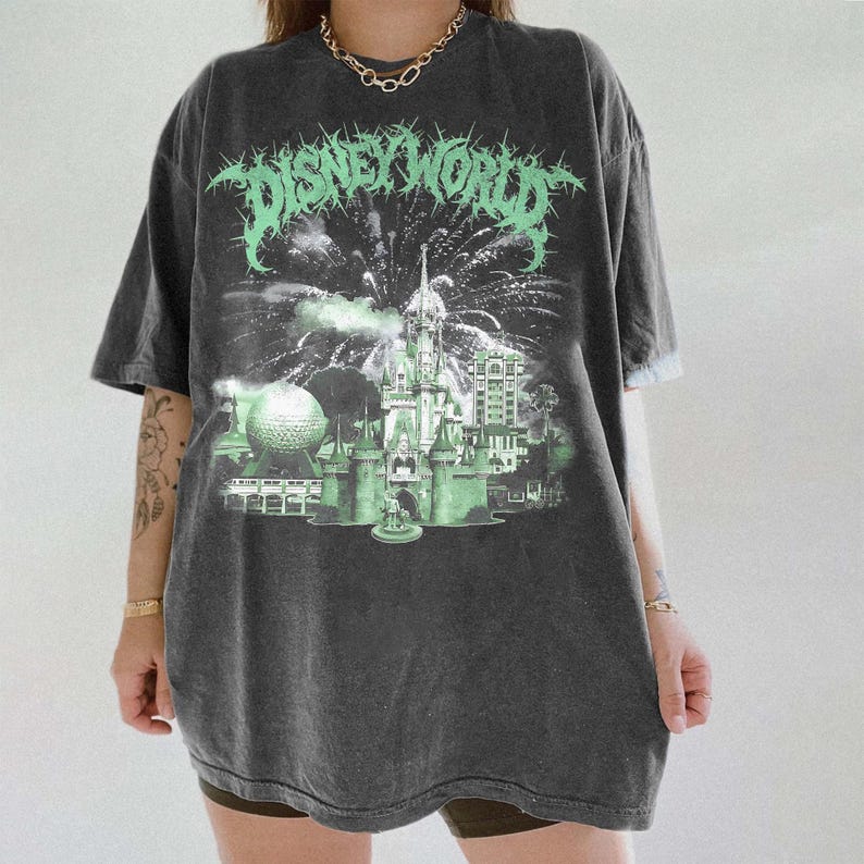 K&ouml;nnte beinhalten: Dunkelgraues T-Shirt mit einem verwaschenen "DISNEY WORLD"-Aufdruck in Neongr&uuml;n. Das Design zeigt ein Schloss, Feuerwerk und Parkelemente. Das Shirt hat kurze &Auml;rmel und eine lockere Passform.