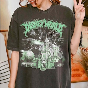 K&ouml;nnte beinhalten: Dunkelgraues T-Shirt mit einem gr&uuml;nen Aufdruck "DISNEY WORLD" in einer stacheligen Schriftart. Die Grafik zeigt ein Schloss, Feuerwerk und einen Golfball. Das Shirt hat eine lockere Passform.