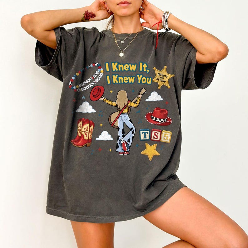 Peut inclure: Un t-shirt gris anthracite avec une impression graphique portant le texte "I Knew It, I Knew You" et "Infinity and Beyond". Le motif comprend un personnage de dessin anim&eacute; avec une guitare, des bottes de cow-boy, un chapeau rouge et des blocs.