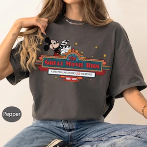 Puede incluir: Camiseta gris oscuro con Mickey Mouse sosteniendo una claqueta de cine. La camiseta muestra el texto "The Great Movie Ride" en un dise&ntilde;o de marquesina, con el texto: "A Spectacular Journey Into The Movies 1989-2017."