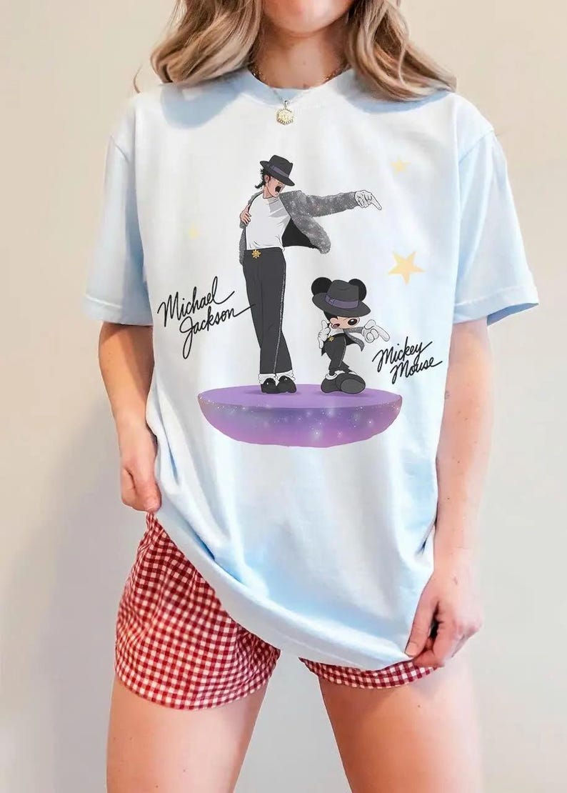 Puede incluir: Camiseta azul claro con un gr&aacute;fico de Michael Jackson y Mickey Mouse. La ilustraci&oacute;n muestra a Michael Jackson con sombrero y traje negro, y a Mickey Mouse con un atuendo similar. La camiseta tiene el texto "Michael Jackson" y "Mickey Mouse".