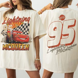 May include: Cream-colored Lightning McQueen t-shirt. The front features a graphic of the red race car, the number 95, and the name McQueen. The back displays a large number 95 and the words "Lightning McQueen".