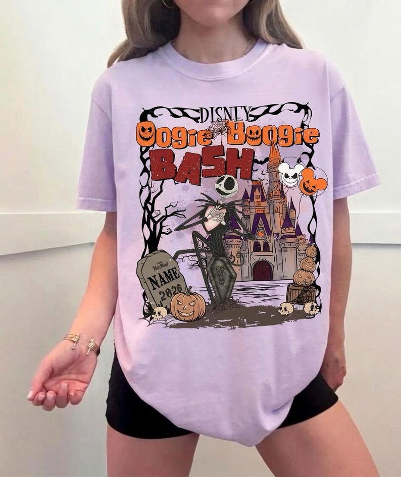 May include: A light purple t-shirt featuring a Halloween-themed graphic. The design includes the text "Disney Oogie Boogie Bash" with Jack Skellington, a castle, pumpkins, and a tombstone. The shirt has short sleeves.
