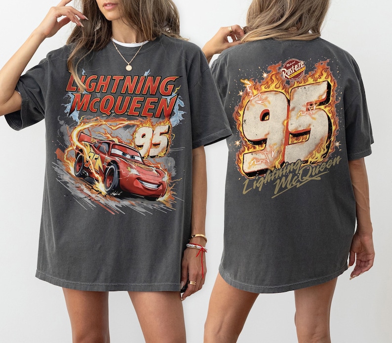 Puede incluir: Camiseta gris oscuro de Lightning McQueen con un gr&aacute;fico del personaje y el n&uacute;mero 95. El dise&ntilde;o frontal muestra el coche corriendo con llamas, mientras que la parte trasera tiene un gran 95 con llamas. Una camiseta de estilo vintage.