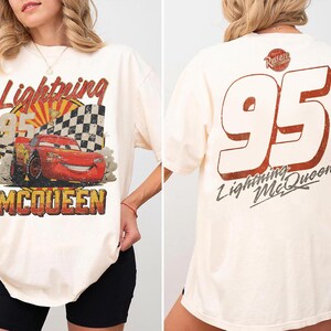May include: Cream-colored t-shirt featuring a graphic of Lightning McQueen from the movie Cars. The front displays the character with the text "Lightning McQueen 95". The back has a large "95" and "Lightning McQueen" text.