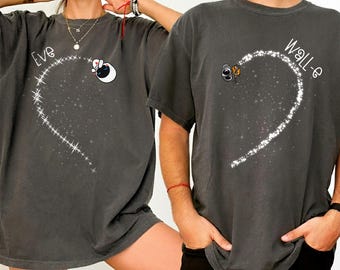 Puede incluir: Dos camisetas gris oscuro con diseños a juego. Una camiseta dice "Eve" con un personaje de dibujos animados y un diseño de corazón brillante. La otra camiseta dice "Wall-e" con un personaje de dibujos animados y un diseño de corazón a juego.