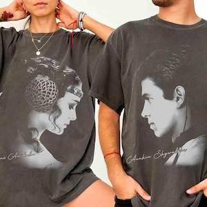 May include: Two dark gray t-shirts featuring black and white portraits. One shirt displays Padmé Amidala with her name below, the other shows Anakin Skywalker with his name. Both shirts have a vintage, worn look.