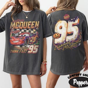 May include: A charcoal gray t-shirt featuring a graphic of Lightning McQueen from Cars on the front with the text Lightning McQueen, Cars, and Think Fast 95. The back displays the number 95 with a pumpkin, a bat, and the text Lightning McQueen.