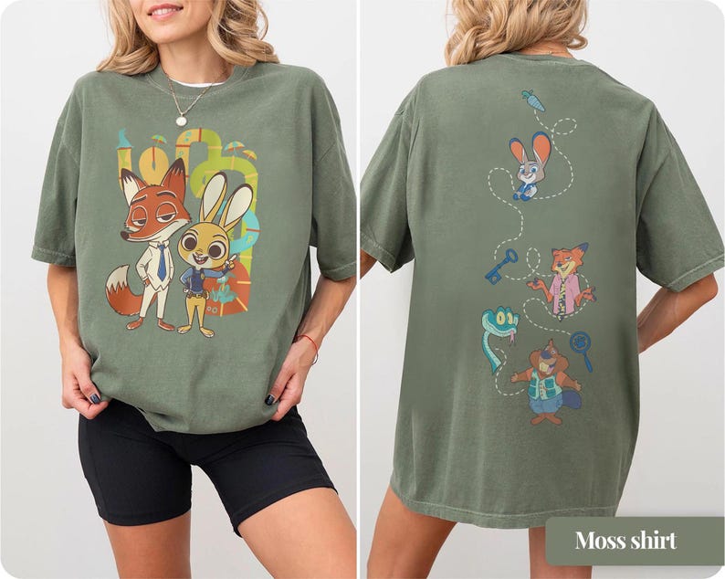 May include: Moss green t-shirt featuring the characters Nick Wilde and Judy Hopps from Zootopia. The front of the shirt displays the characters, while the back showcases other characters and objects from the movie. The shirt is made of a soft material.