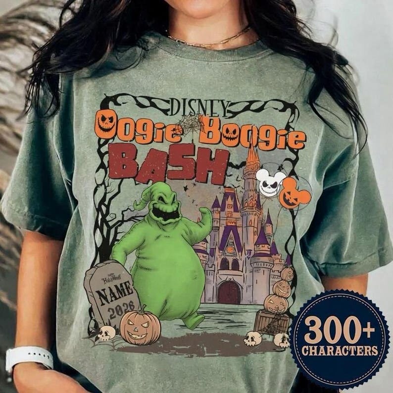 May include: Sage green t-shirt featuring a graphic for the Disney Oogie Boogie Bash. The design includes the text "Disney Oogie Boogie Bash" in orange and red, with a cartoon character, pumpkins, and a castle. The shirt has a crew neck and short sleeves.