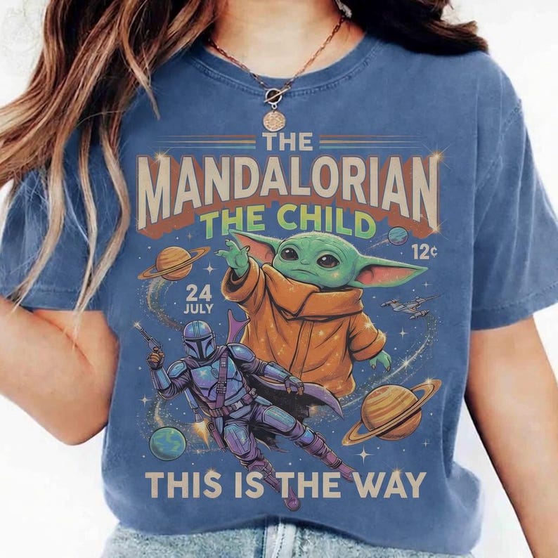 May include: Blue t-shirt featuring a graphic of The Mandalorian and The Child (Grogu) from the Star Wars series. The design includes planets, a spaceship, and the text "THIS IS THE WAY".