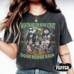 Puede incluir: Camiseta gris oscuro con un gr&aacute;fico colorido de la pel&iacute;cula "Pesadilla antes de Navidad". El dise&ntilde;o incluye a Jack Skellington, Sally y otros personajes, con el texto "Nightmare on Main Street EST 2025 OOGIE BOOGIE BASH."