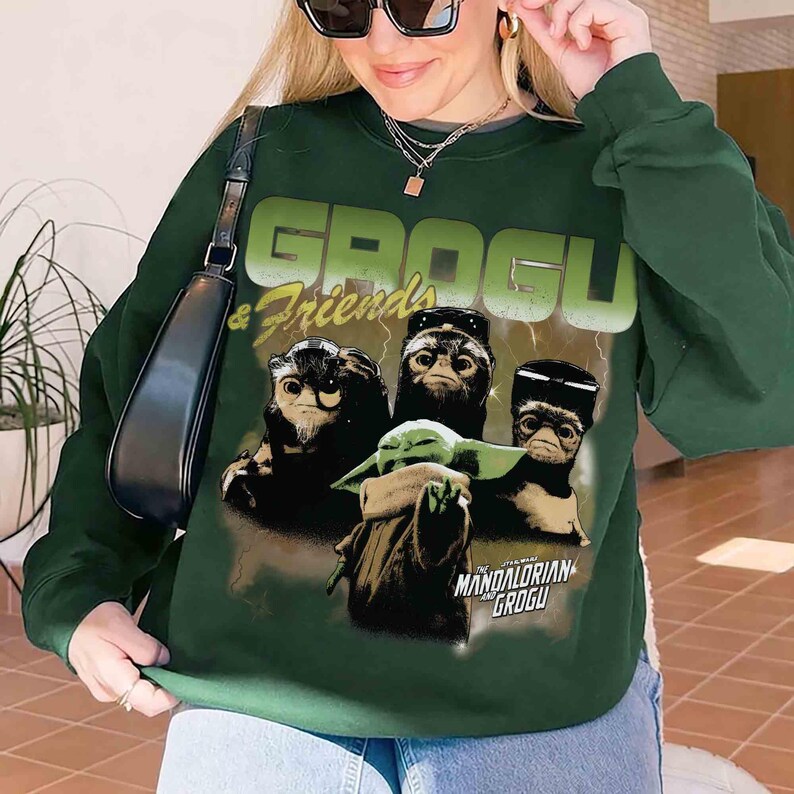 Pu&ograve; includere: Felpa verde scuro con una grafica di Grogu e amici da The Mandalorian. Il design include il testo "GROGU & Friends" in un carattere verde chiaro, con "MANDALORIAN GROGU" sotto. La felpa &egrave; uno stile girocollo.