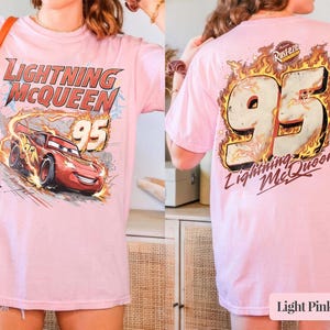 Puede incluir: Camiseta rosa claro con Lightning McQueen y el n&uacute;mero 95. El frente muestra el coche de carreras rojo, llamas y el texto "Lightning McQueen". La parte trasera presenta el n&uacute;mero 95 en llamas y el texto "Lightning McQueen".