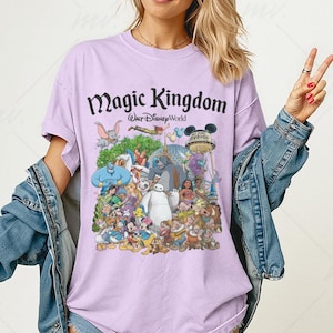 Puede incluir: Camiseta lila con un estampado colorido de personajes de Disney. Las palabras "Magic Kingdom Walt Disney World" est&aacute;n impresas en negro. La camiseta tiene mangas cortas y un corte holgado, ideal para un look casual.
