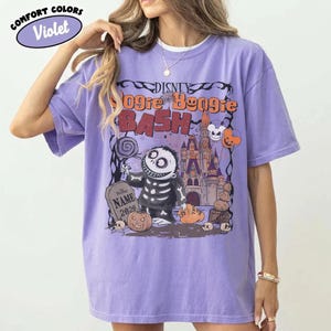 May include: Violet Comfort Colors t-shirt featuring a graphic for the Disney Oogie Boogie Bash. The design includes Jack Skellington, a tombstone, and a castle. The text "Disney Oogie Boogie Bash" is displayed across the top.