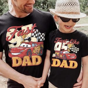 May include: Black t-shirts with matching designs. One shirt says "Fast 95 DAD" with a red race car graphic, a trophy, and a checkered flag. The other says "Fast like 05 DAD" with a similar design.