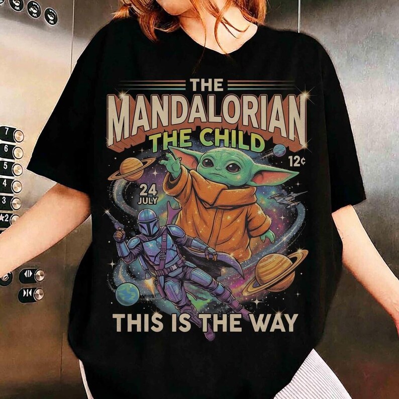 May include: Black t-shirt featuring a graphic from The Mandalorian. The design includes the text "THE MANDALORIAN THE CHILD" with an image of Grogu and the Mandalorian. The text "THIS IS THE WAY" is also included.