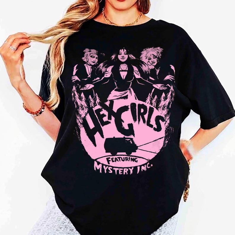 May include: Black t-shirt featuring a pink graphic of three women and a van, with the text "HEX GIRLS" and "FEATURING MYSTERY INC." The design is set within a pink circle. The shirt is a casual wear item.