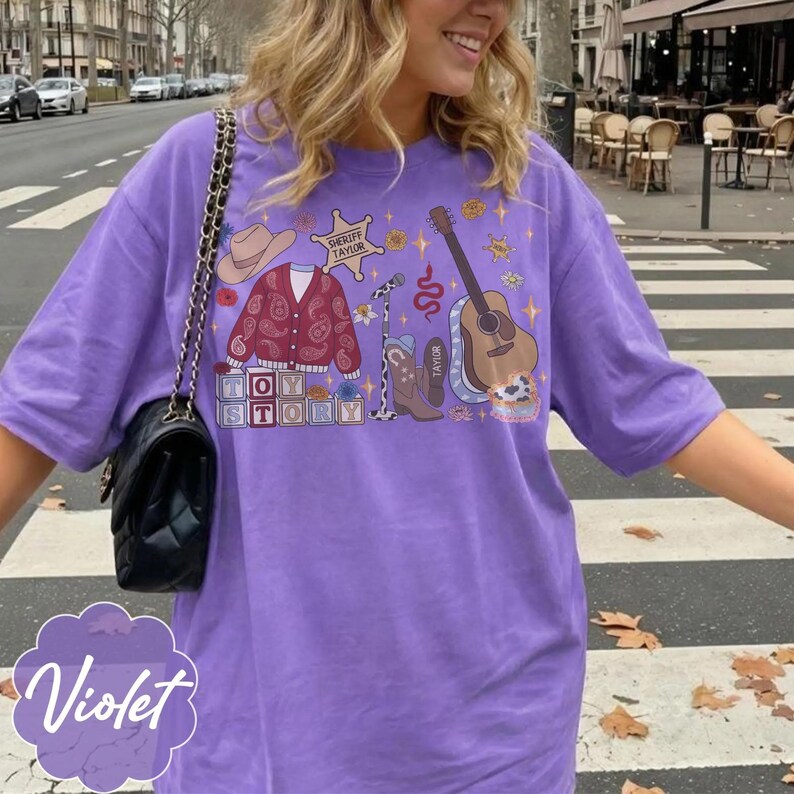 May include: A violet t-shirt featuring a graphic print with a cowboy hat, a paisley cardigan, a sheriff badge labeled Sheriff Taylor, a microphone, a guitar, a cowboy boot labeled Taylor, and blocks spelling Toy Story with stars and flowers.
