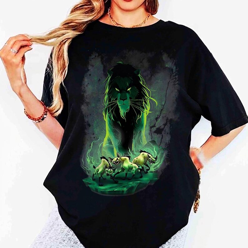 Puede incluir: Camiseta negra con una ilustraci&oacute;n verde y negra de un le&oacute;n con ojos y melena brillantes, rodeado de niebla verde. Debajo del le&oacute;n hay tres hienas sobre una plataforma verde. El dise&ntilde;o es una impresi&oacute;n gr&aacute;fica.