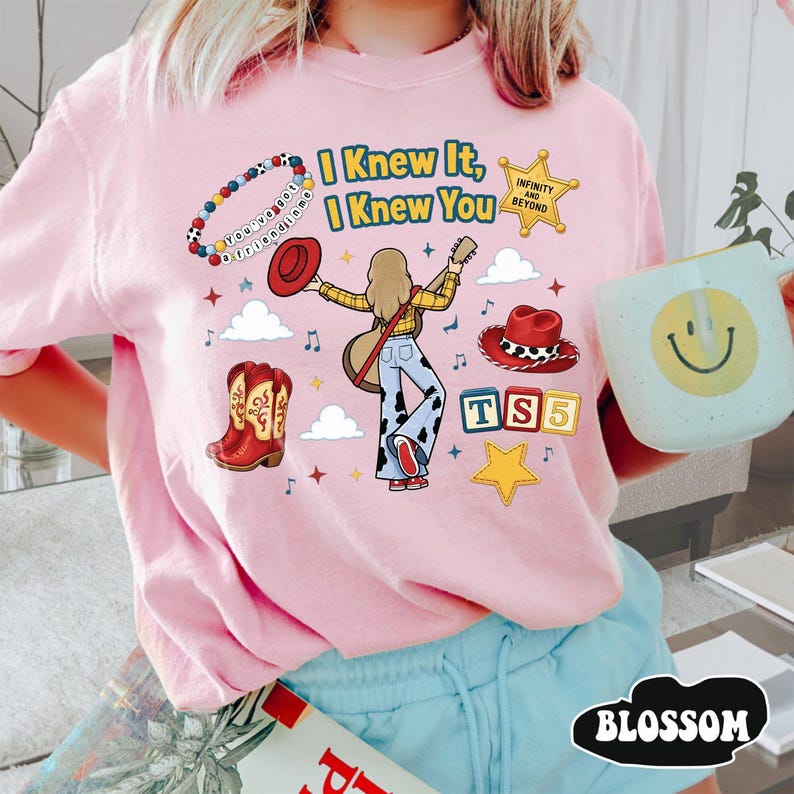 Peut inclure: Un t-shirt rose clair avec une impression graphique portant le texte I Knew It, I Knew You, un bracelet de perles, une &eacute;toile de sh&eacute;rif, un chapeau de cowboy rouge, une guitare, un pantalon &agrave; motif vache, une botte rouge et une &eacute;toile jaune.