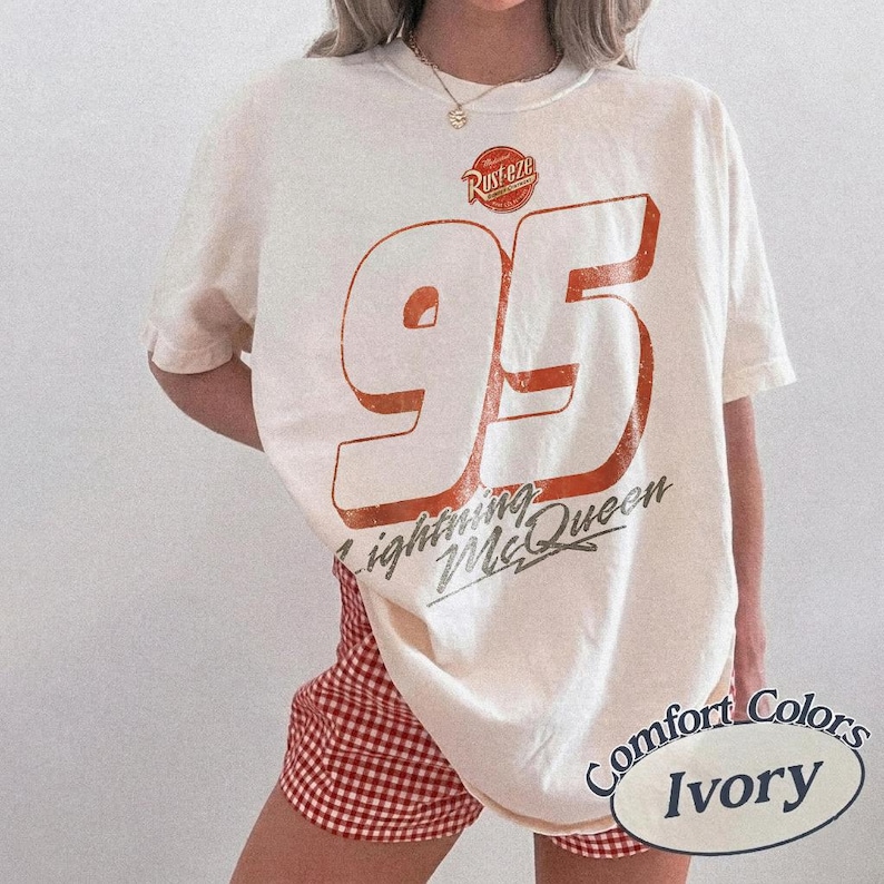 Puede incluir: Camiseta de color marfil con un gran n&uacute;mero 95 naranja y las palabras "Lightning McQueen" y "Rusteze". La camiseta tiene un aspecto vintage y desgastado. La esquina inferior derecha de la camiseta tiene las palabras "Comfort Colors" e "Ivory".