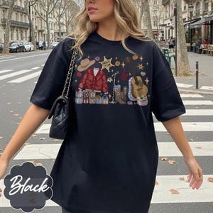 May include: A black t-shirt featuring a graphic print of a brown cowboy hat, a red paisley cardigan, a sheriff badge labeled Taylor, a guitar, a cowboy boot, and blocks spelling Toy Story, accented with small stars and floral elements.