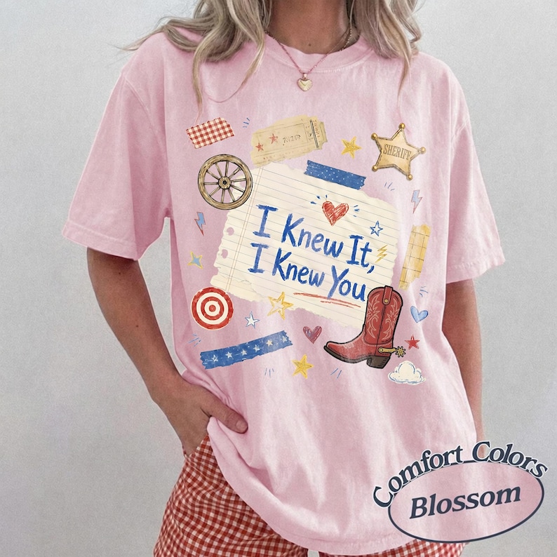 May include: A light pink short-sleeve t-shirt featuring a graphic print of a lined notebook paper with the text I Knew It, I Knew You, a red cowboy boot, a sheriff star, a wagon wheel, a target, and various small decorative shapes and patterns.