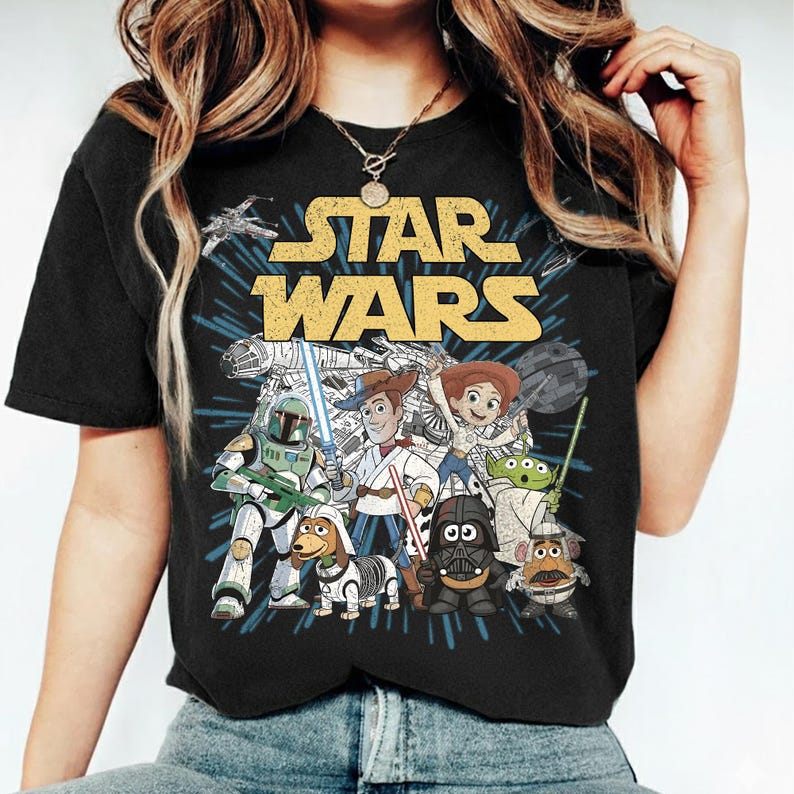 Puede incluir: Camiseta negra con un gr&aacute;fico de personajes de Star Wars, incluyendo Darth Vader, Woody y Buzz Lightyear. El logo de Star Wars es amarillo. El dise&ntilde;o incluye un fondo azul en r&aacute;faga.