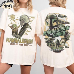 K&ouml;nnte beinhalten: Elfenbeinfarbene T-Shirts mit "The Mandalorian" und Grogu. Das Frontdesign zeigt den Mandalorianer und Grogu mit dem Text "MANDALORIAN - THIS IS THE WAY". Das R&uuml;ckendesign enth&auml;lt den Text "STAR WARS THE MANDALORIAN AND GROGU - THIS IS THE WAY".