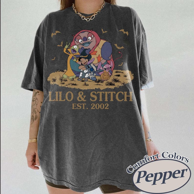 May include: Dark gray t-shirt featuring a colorful graphic of Lilo & Stitch characters with the text "LILO & STITCH EST. 2002". The shirt has a vintage look and the Comfort Colors Pepper logo.