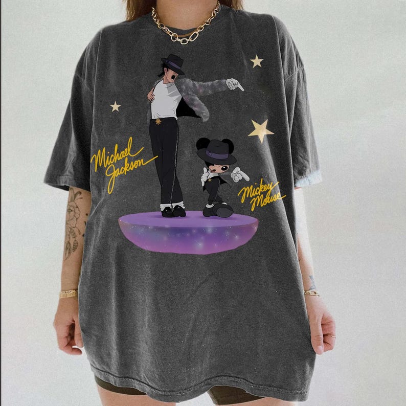 Puede incluir: Camiseta gris oscuro con un gr&aacute;fico de Michael Jackson y Mickey Mouse en una plataforma p&uacute;rpura. Los textos "Michael Jackson" y "Mickey Mouse" est&aacute;n en escritura amarilla. La camiseta tiene un corte holgado.
