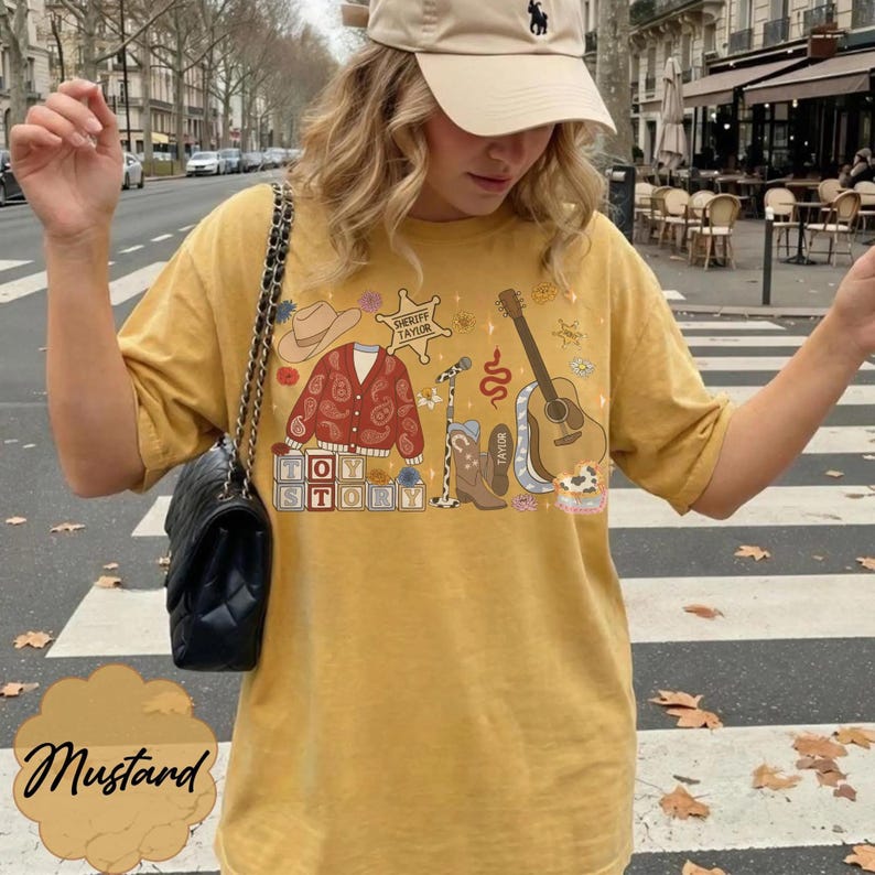 May include: A mustard yellow short-sleeve t-shirt featuring a graphic print of a cowboy hat, a paisley cardigan, a sheriff badge labeled "Sheriff Taylor," a microphone, a cowboy boot, a guitar, and blocks spelling "Toy Story."