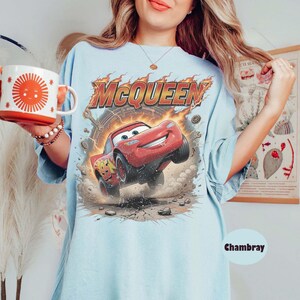 Op de afbeelding: Lichtblauw T-shirt met een afbeelding van Bliksem McQueen uit de film Cars. Het ontwerp bevat de naam "McQueen" in vlammen en het nummer 95 op de auto. Het shirt heeft een losse pasvorm.