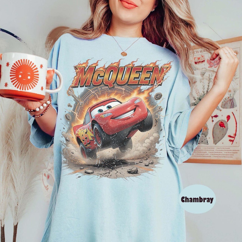Op de afbeelding: Lichtblauw T-shirt met een afbeelding van Bliksem McQueen uit de film Cars. Het ontwerp bevat de naam "McQueen" in vlammen en het nummer 95 op de auto. Het shirt heeft een losse pasvorm.