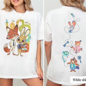 May include: White t-shirt featuring a cartoon illustration of a fox and a rabbit. The front of the shirt displays the characters in a colorful design. The back of the shirt has additional cartoon characters and the text "White shirt".