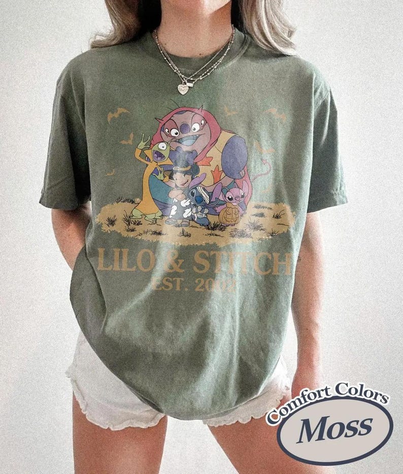 May include: Olive green t-shirt featuring a graphic of characters from Lilo & Stitch, with the text "Lilo & Stitch EST. 2002". The shirt is a Comfort Colors brand.