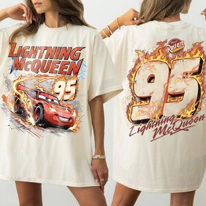 Puede incluir: Camiseta color crema con Lightning McQueen de la pel&iacute;cula Cars. El gr&aacute;fico frontal muestra a McQueen corriendo con el texto "Lightning McQueen 95". La parte trasera muestra un gran "95" en llamas con "Lightning McQueen" debajo.