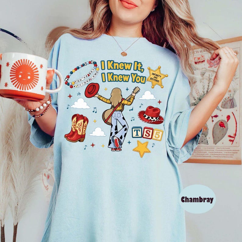 Peut inclure: Un t-shirt bleu clair avec une impression graphique portant le texte "I Knew It, I Knew You", un personnage de dessin anim&eacute; jouant de la guitare, un chapeau de cowboy rouge, des bottes de cowboy rouges, un bracelet de perles et des blocs "TS5".
