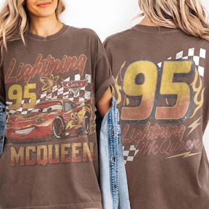 May include: Brown t-shirt featuring Lightning McQueen from the Cars movie. The front graphic includes the number 95, the character's name, and a checkered flag. The back of the shirt also displays the number 95 and the words "Lightning McQueen".