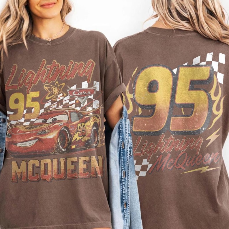 May include: Brown t-shirt featuring Lightning McQueen from the Cars movie. The front graphic includes the number 95, the character's name, and a checkered flag. The back of the shirt also displays the number 95 and the words "Lightning McQueen".