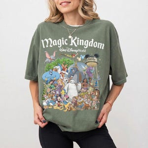 Puede incluir: Camiseta verde con un gr&aacute;fico colorido de personajes de Disney y el texto "Magic Kingdom Walt Disney World". El dise&ntilde;o incluye personajes como Mickey Mouse, Aladdin y Baymax. La camiseta tiene mangas cortas y cuello redondo.