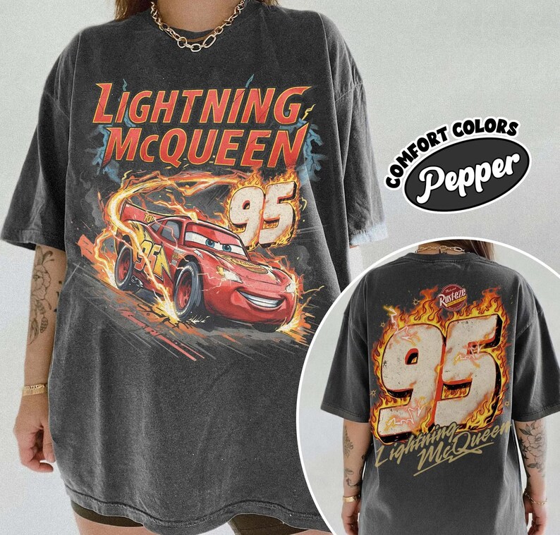 Puede incluir: Camiseta gris oscuro de Lightning McQueen con un coche de carreras rojo y el n&uacute;mero 95. El dise&ntilde;o frontal incluye el texto "Lightning McQueen" en rojo y naranja. La parte trasera de la camiseta tambi&eacute;n muestra el n&uacute;mero 95 y "Lightning McQueen".