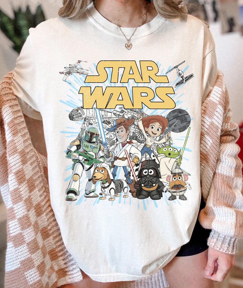 Puede incluir: Camiseta gr&aacute;fica de Star Wars de color crema con el logotipo de Star Wars y varios personajes de la franquicia. El dise&ntilde;o incluye personajes como Darth Vader, Yoda y Woody.